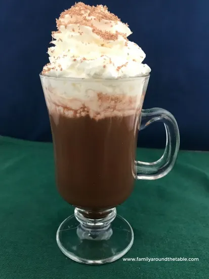 A mug of hot chocolate topped with whipped cream and chocolate shavings.