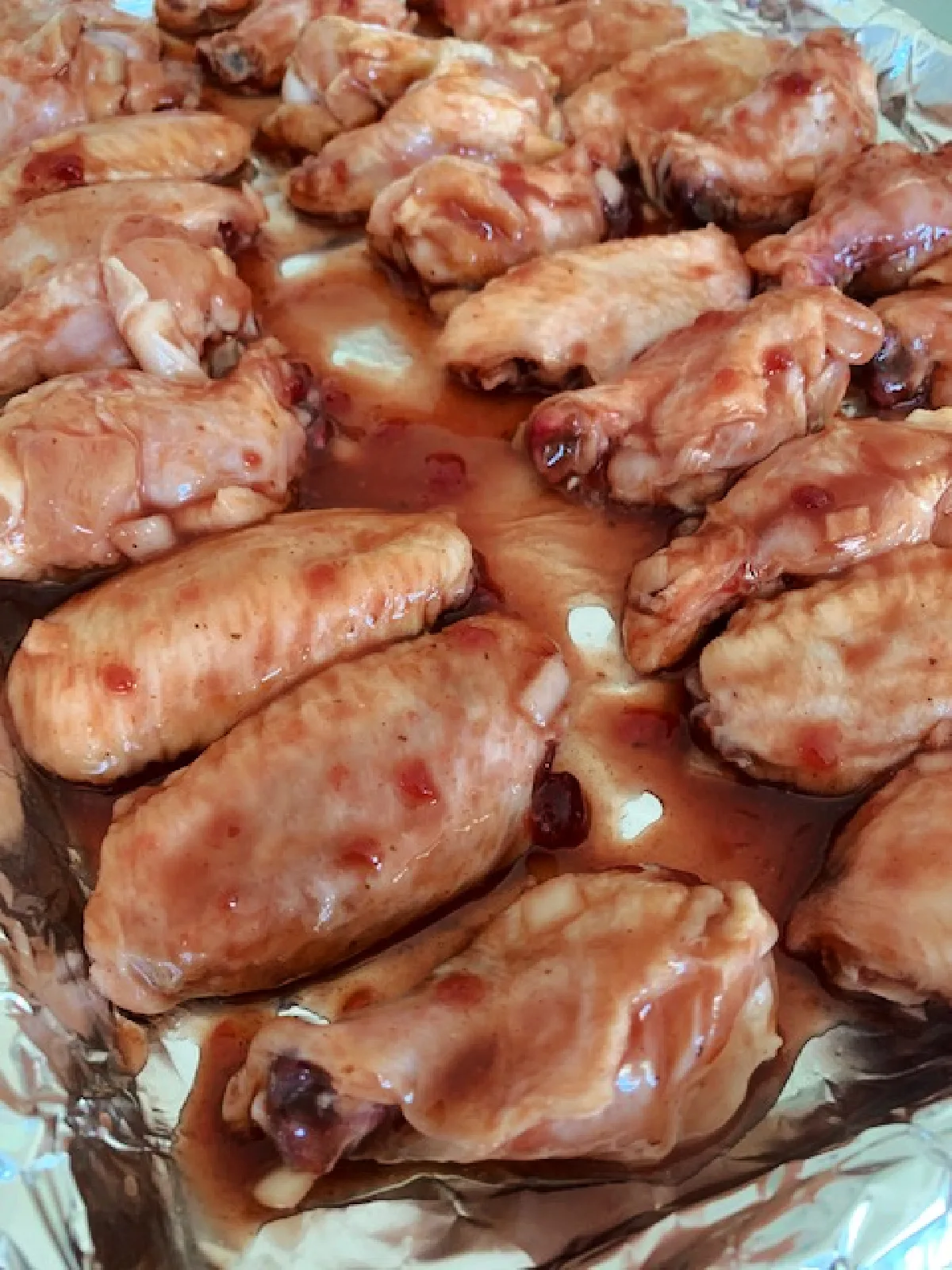 Chicken wings on a baking sheet covered in a sauce ready for the oven.