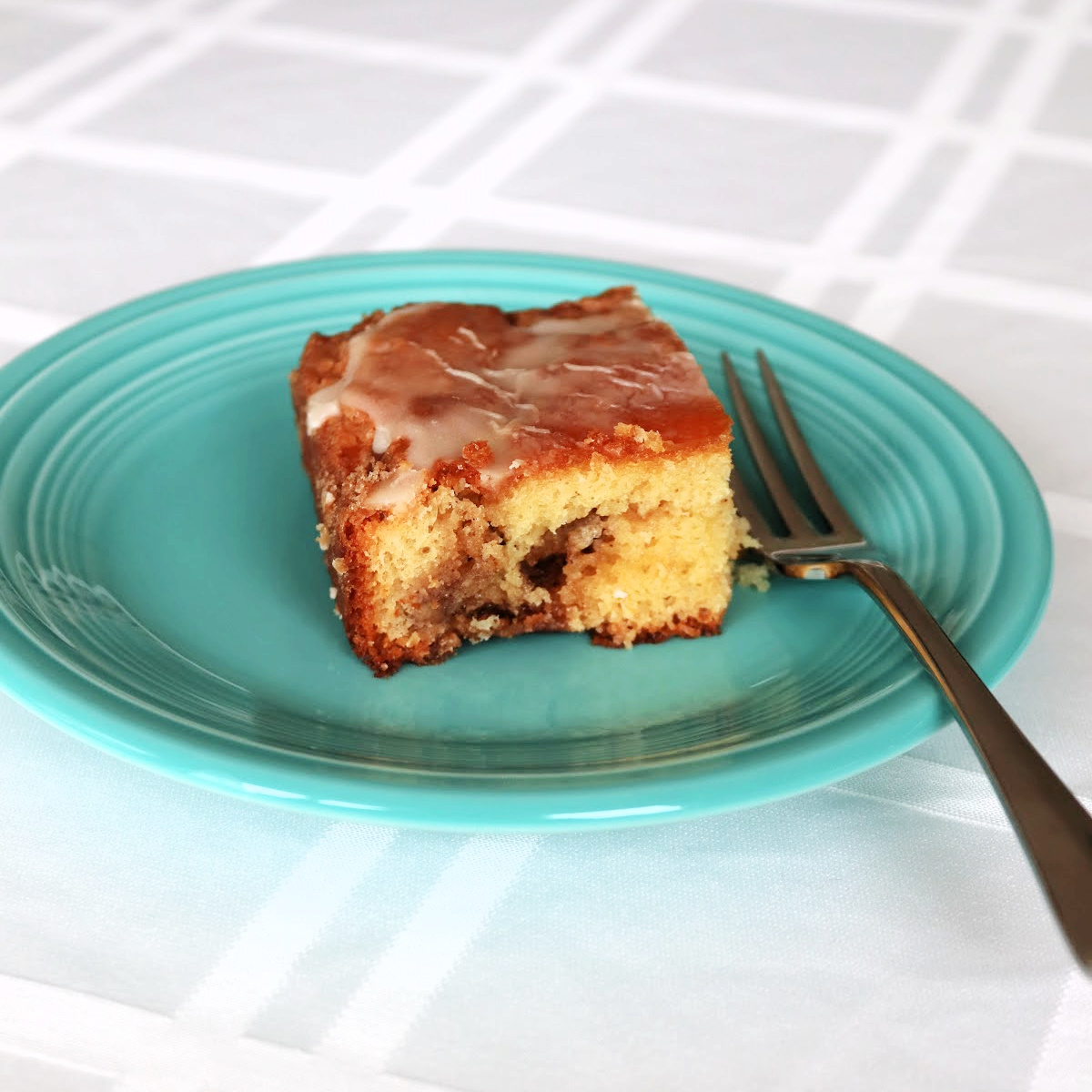 A slice of honey bun cake on a teal plate with a fork next to it.