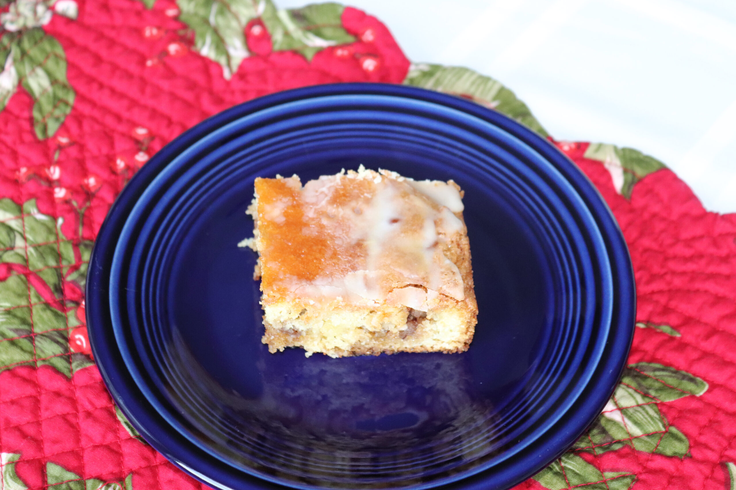 A slice of honey bun cake on a navy blue plate on a red placemat.