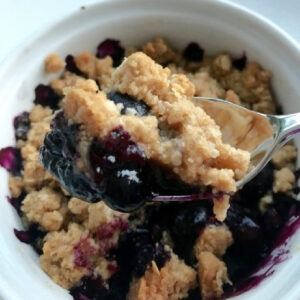 Blueberry Crisp for Two in a white ramekin with a portion on a silver spoon.