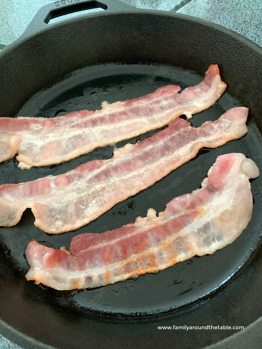Bacon frying in a cast iron skillet.