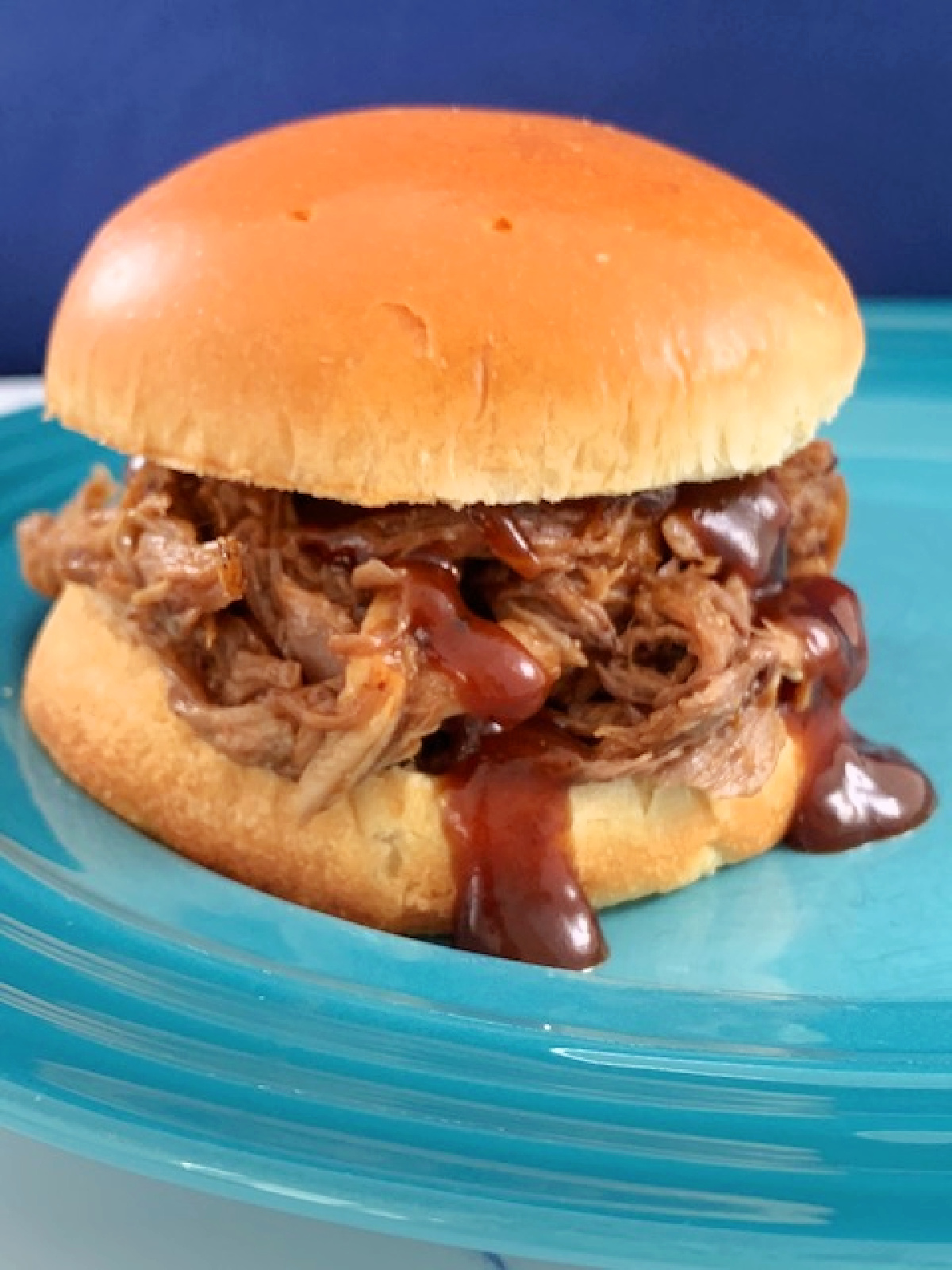 Side view of a pulled pork sandwich with barbecue sauce drips.