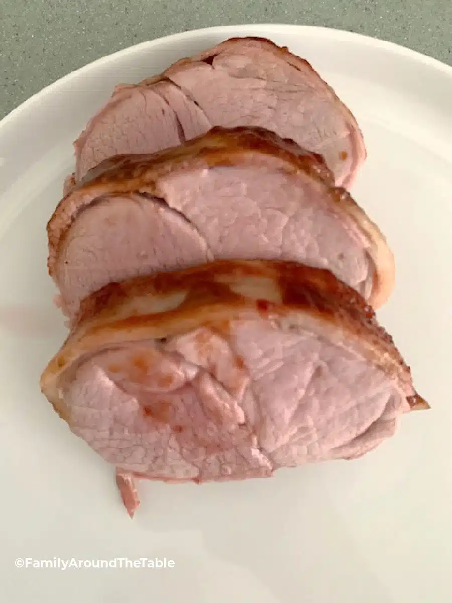 Slices of honey barbecue bacon wrapped pork tenderloin on a white plate.
