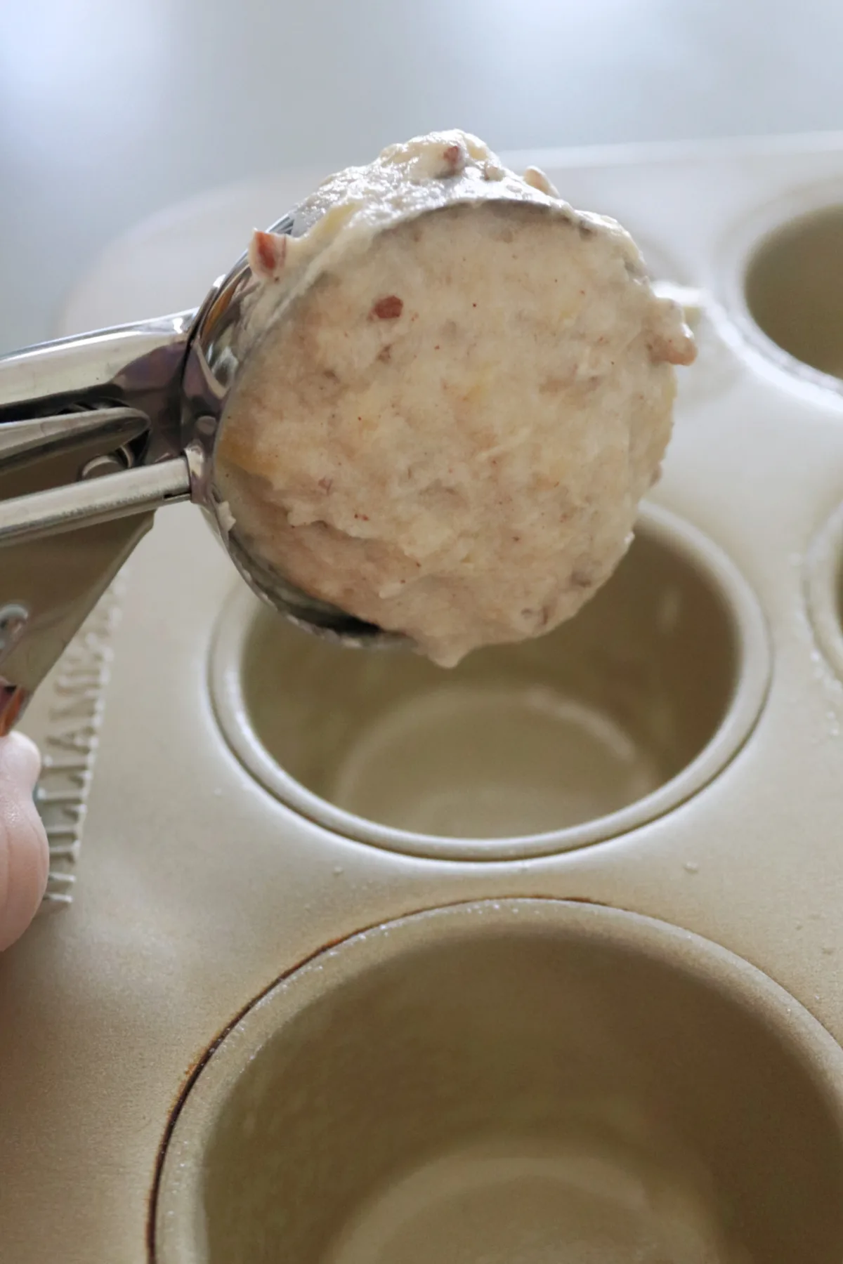 Batter in a scoop being put into a muffin tin.