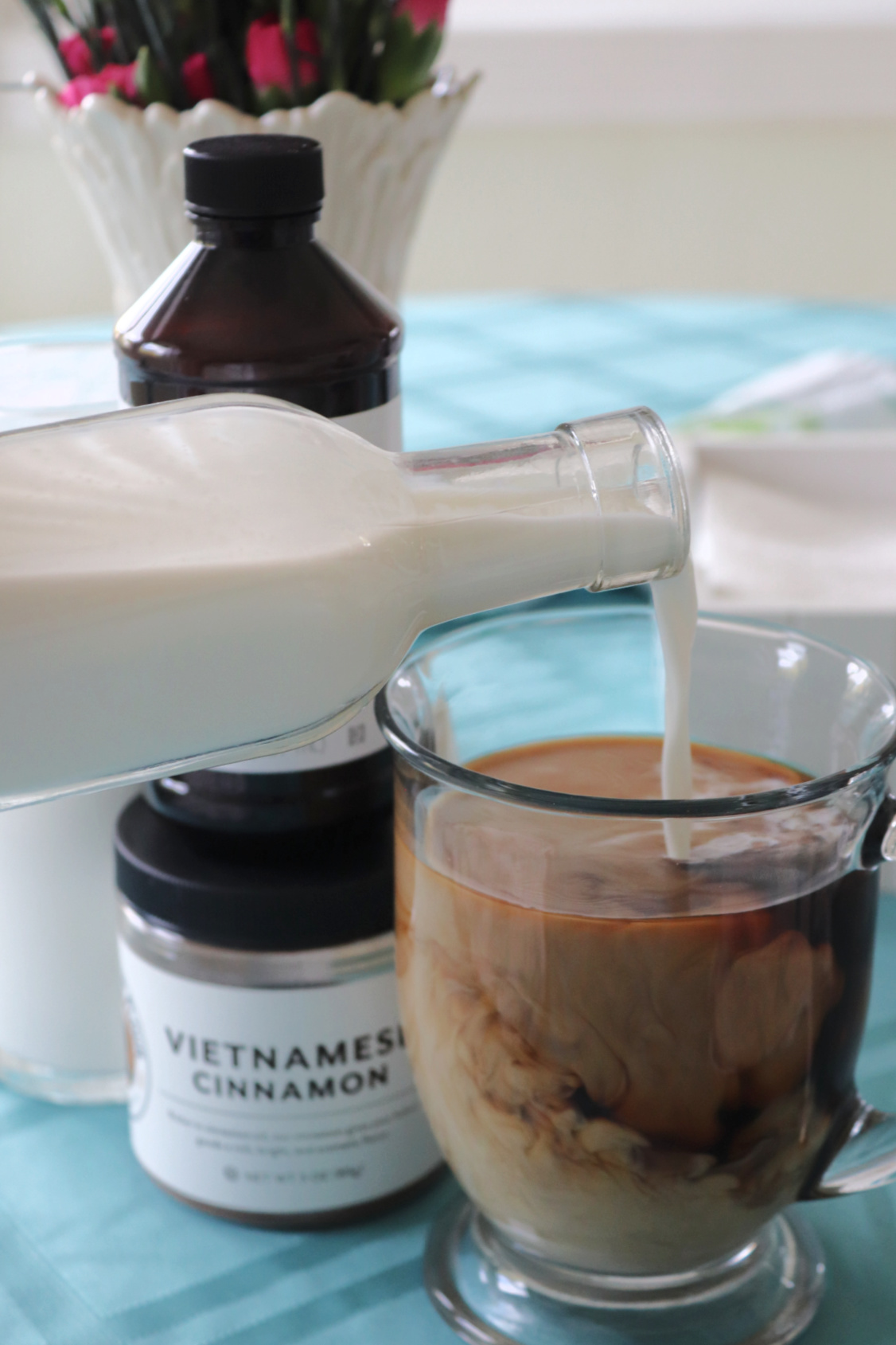 Creamer being poured into a cup of coffee from a glass bottle.