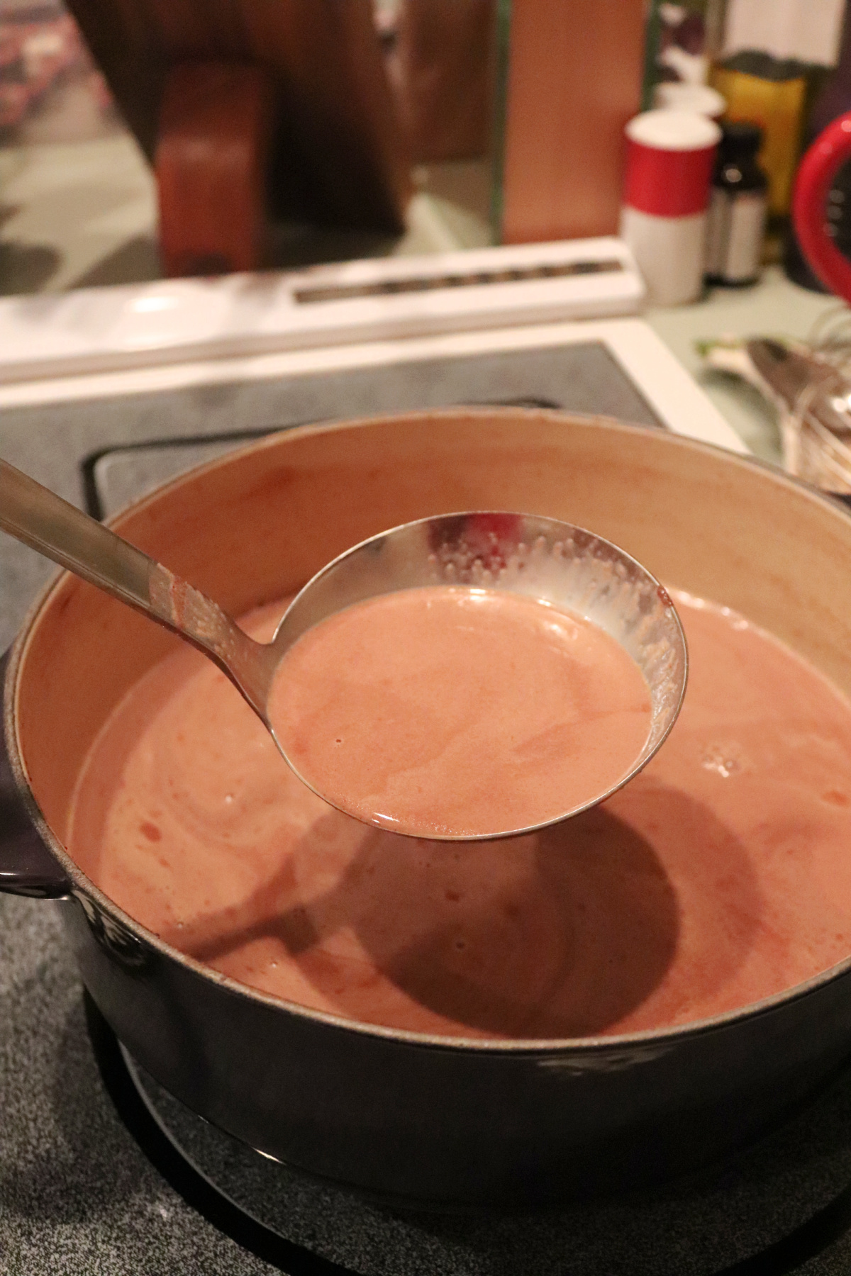 Hot chocolate in a ladle over a pot on the stove.