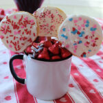 Three cookie pops in a mug with red candy.