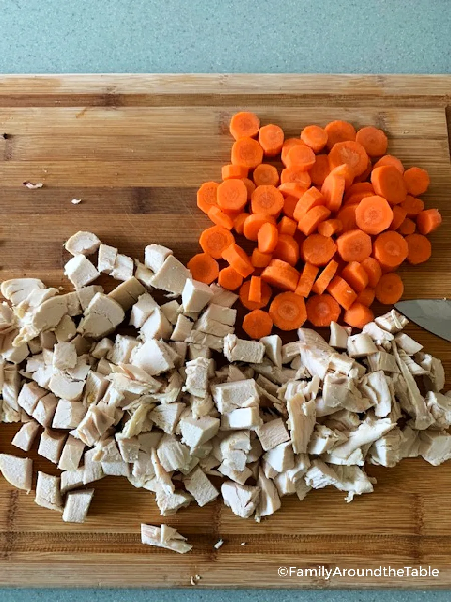 Cubed chicken and sliced carrots on a cutting board.