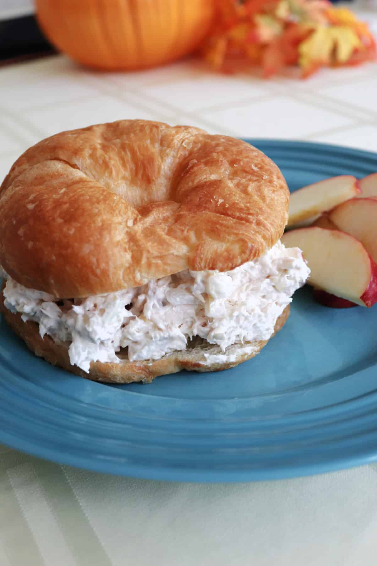 Easy Apple Chicken Salad on a croissant on a blue plate with apple slices.