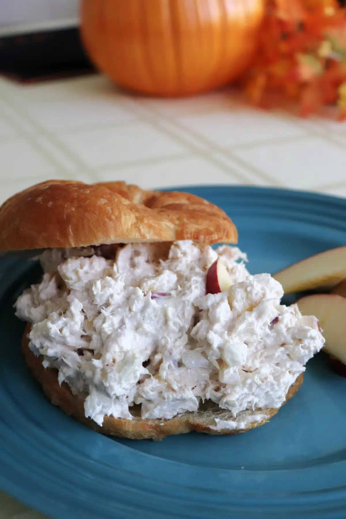 Easy Apple Chicken Salad on a croissant on a blue plate with apple slices.