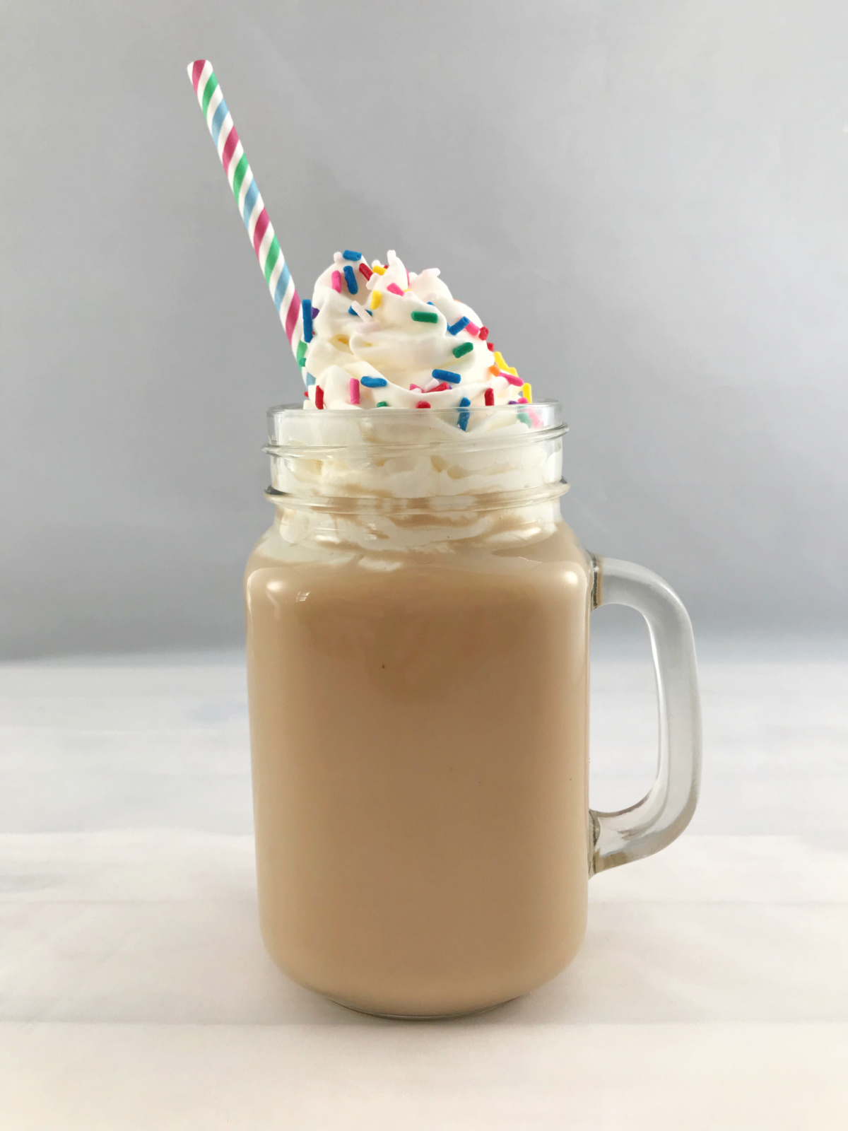 Iced Birthday Cake Latte in a glass mug with whipped cream and sprinkles.