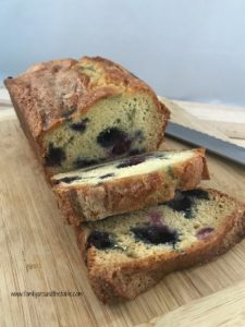 Homemade blueberry orange bread sliced on a cutting board with a knife in the background.