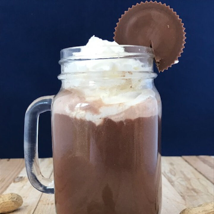 Spiked peanut butter hot chocolate in a mug glass with whipped cream and a peanut butter cup as a garnish.