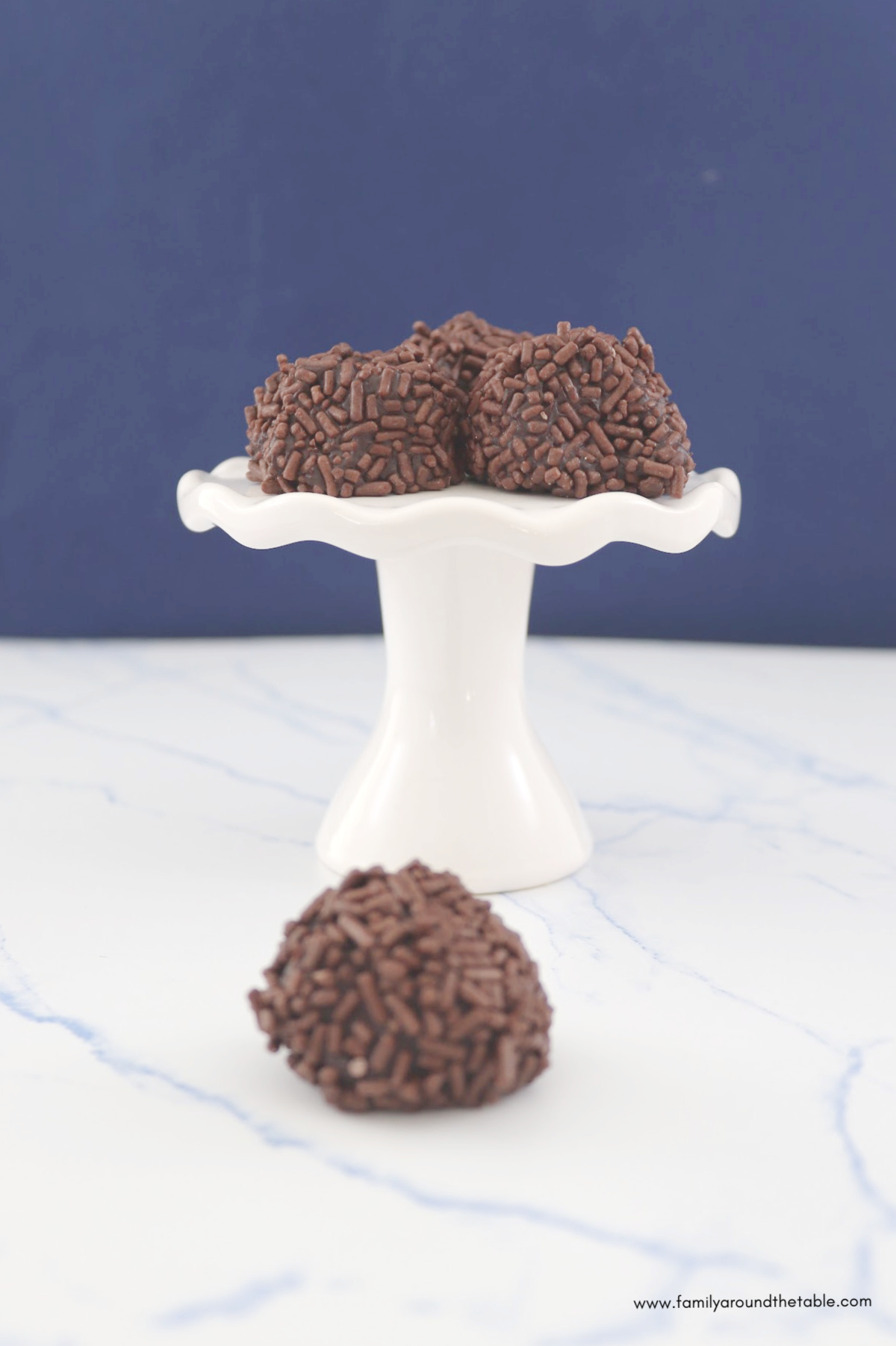 Dark chocolate raspberry almond truffles with sprinkles on a white pedestal plate.