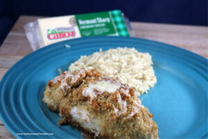 Broccoli and Cheddar chicken roll-up on a plate with rice and a block of Cabot cheddar cheese in the background.