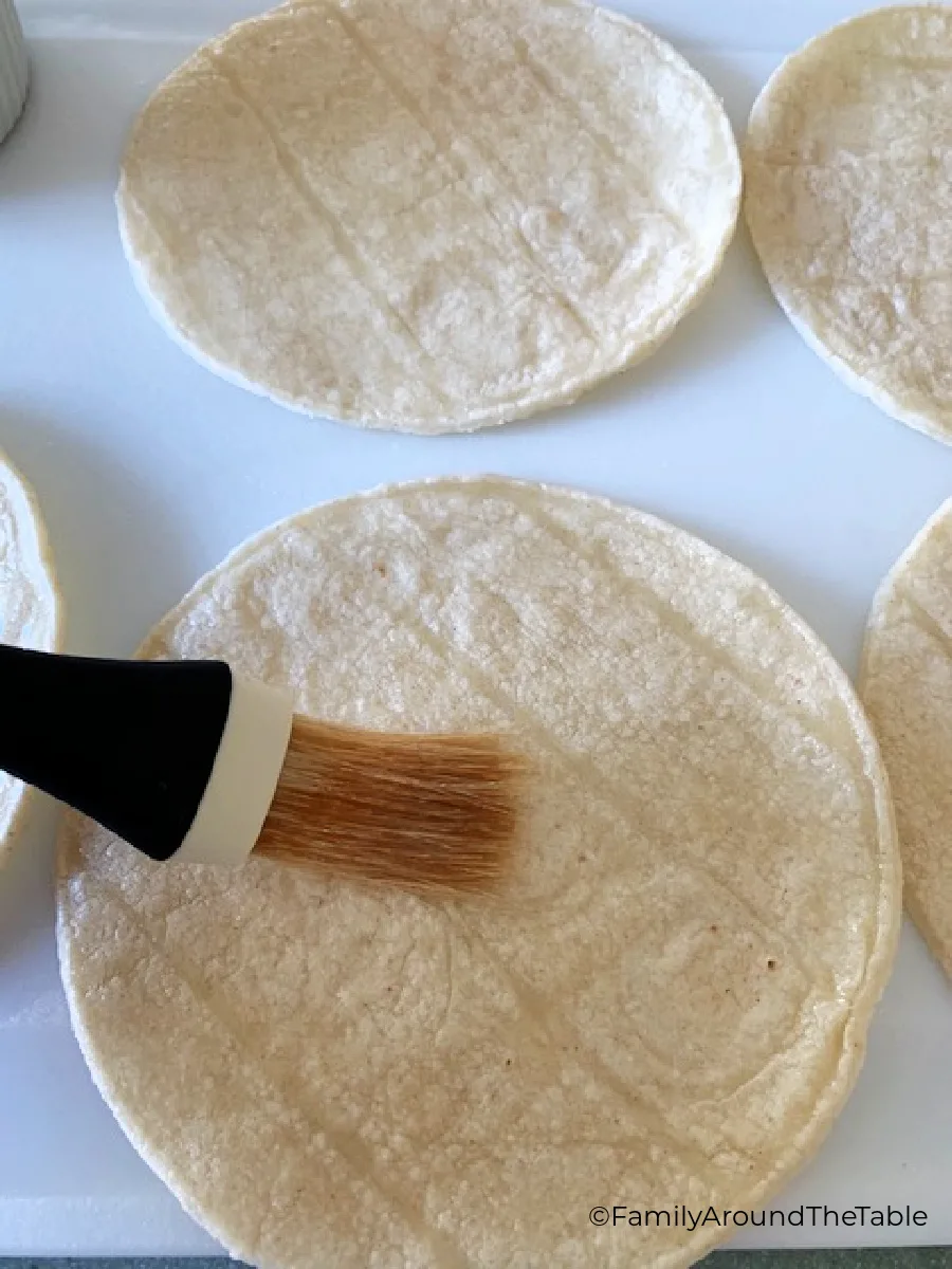 A corn tortilla on a white surface being brushed with oil.