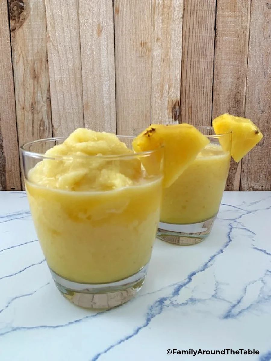 Two frozen pineapple margaritas on a marbled surface.