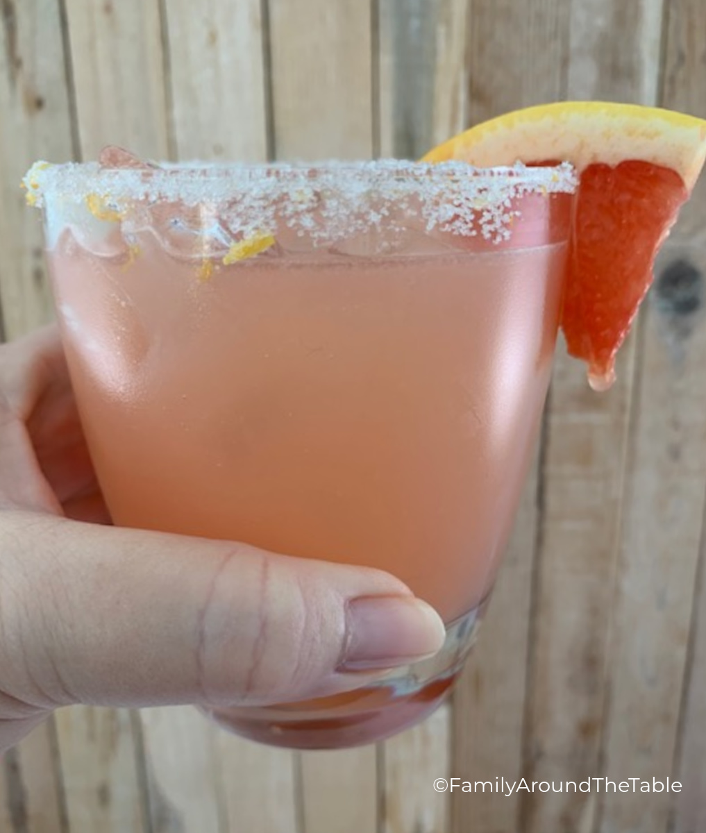A cocktail garnished with a grapefruit wedge being held.