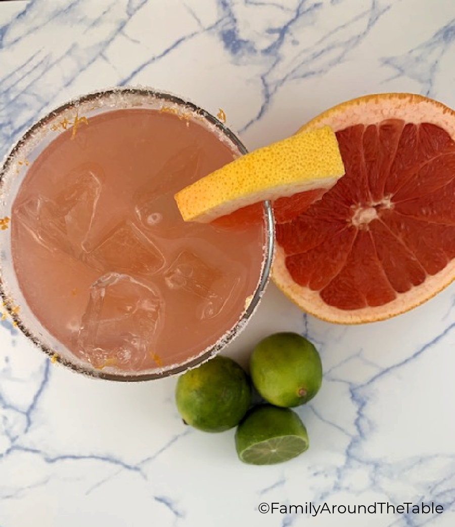 Overhead photo of a cocktail with limes and half a ruby red grapefruit.