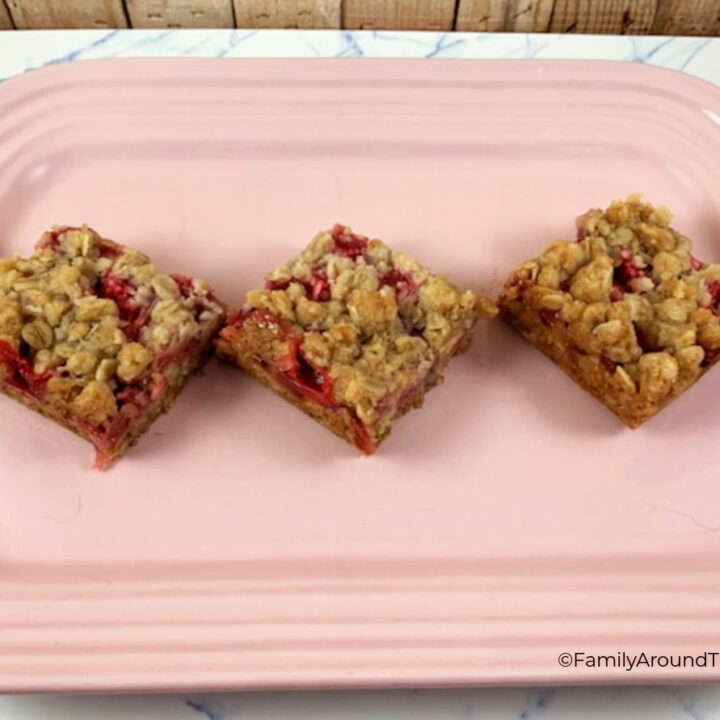 Three strawberry rhubarb oat bars on a pink platter.