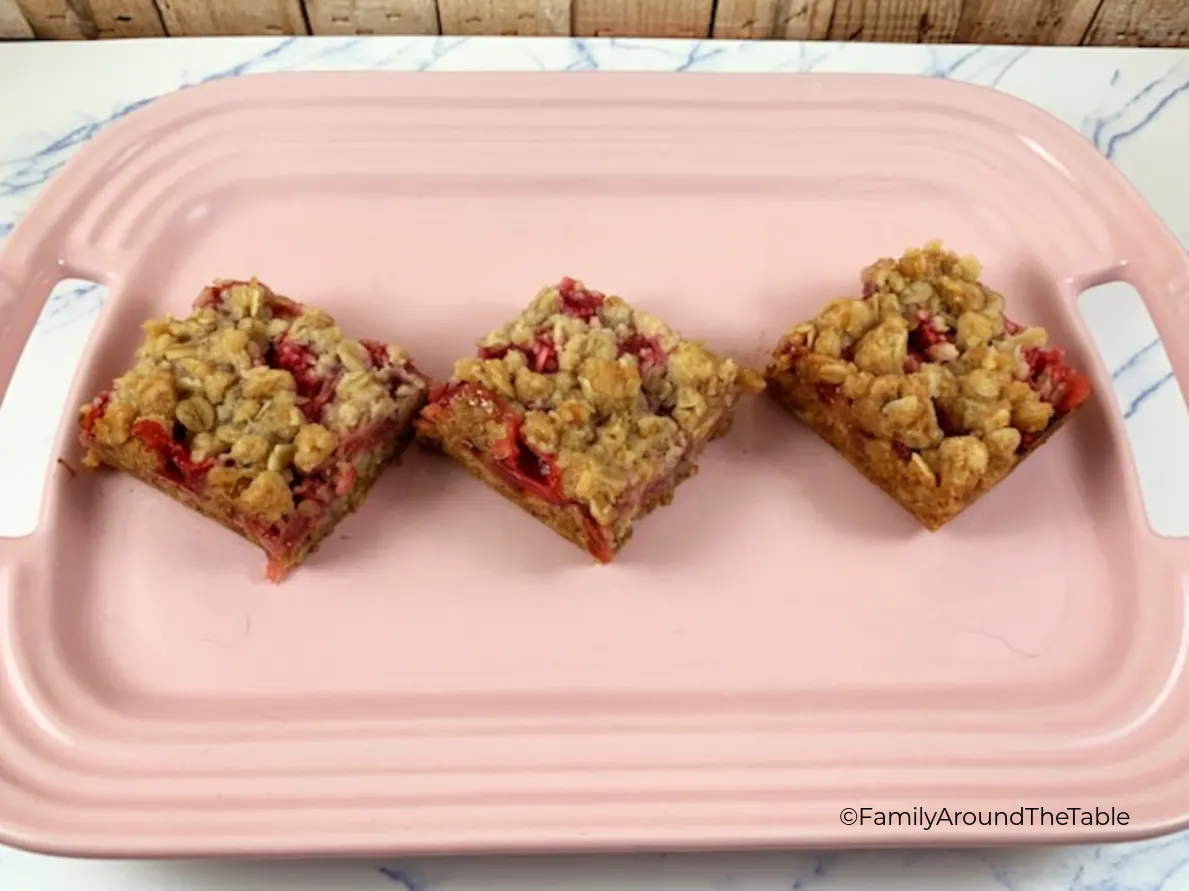 Three strawberry rhubarb oat bars on a pink platter.
