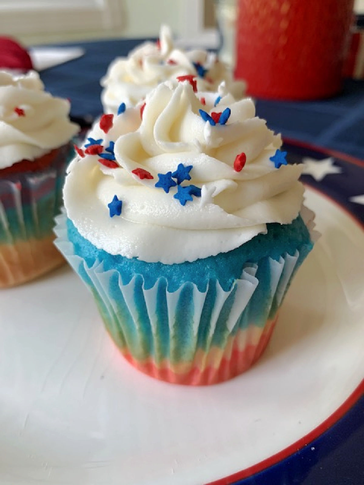 A red, white, and blue cupcake with white frosting and sprinkles of a plate.