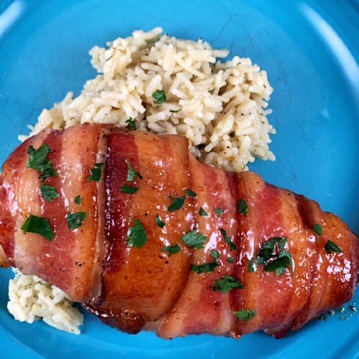 A chicken breast wrapped in bacon sitting on rice on a blue plate.