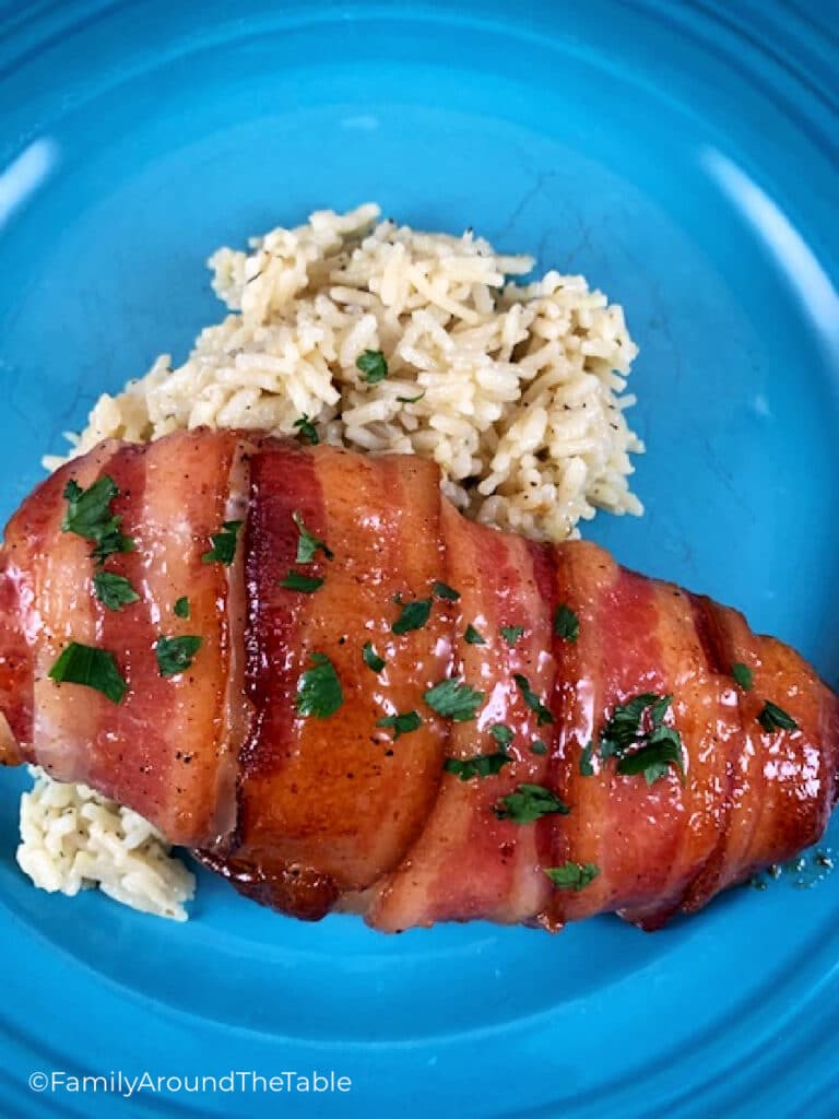 A chicken breast wrapped in bacon sitting on rice on a blue plate.