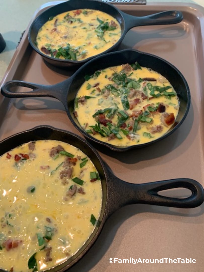 3 individual cast iron skillets with eggs in them on a baking sheet.
