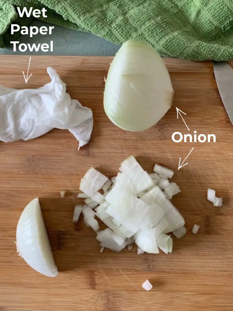 Overhead view of a cutting board with a wet paper towel and onions.