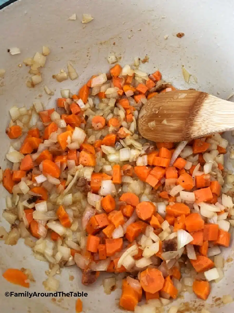 Carrots and onions sauteeing in a Dutch oven.