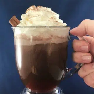 A mug of Mexicocoa with whipped cream being held by the handle.