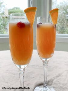 Two mimosas in champagne glasses garnished with an orange and cranberries.