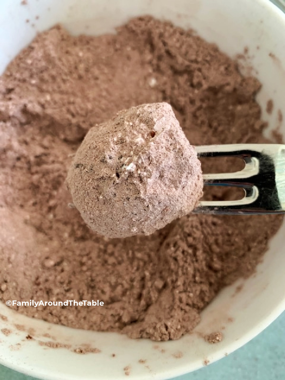 Cookie on a fork over a bowl filled with cocoa and powdered sugar.