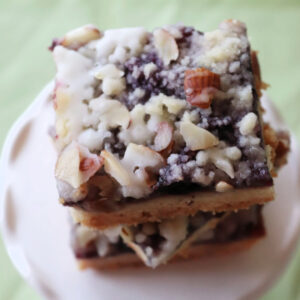 Three blueberry lemon bars stacked on a white plate.