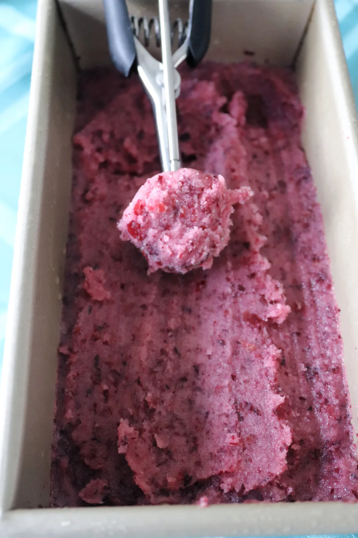 Grape sorbet in a loaf pan with a scoop laying on top.