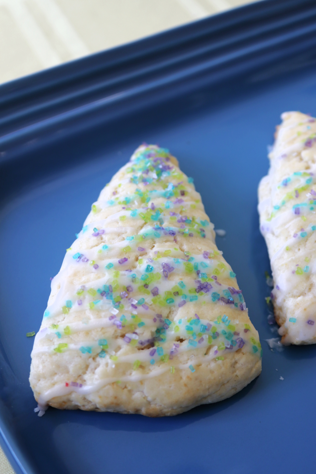 Lemon scones with lavender glaze and colored sugar on a blue platter.
