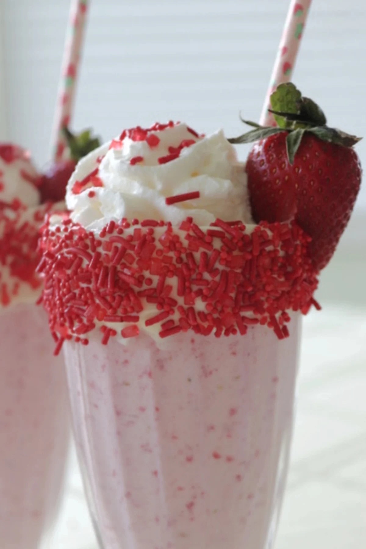 A strawberry milkshake with whipped cream and sprinkles garnished with a strawberry.
