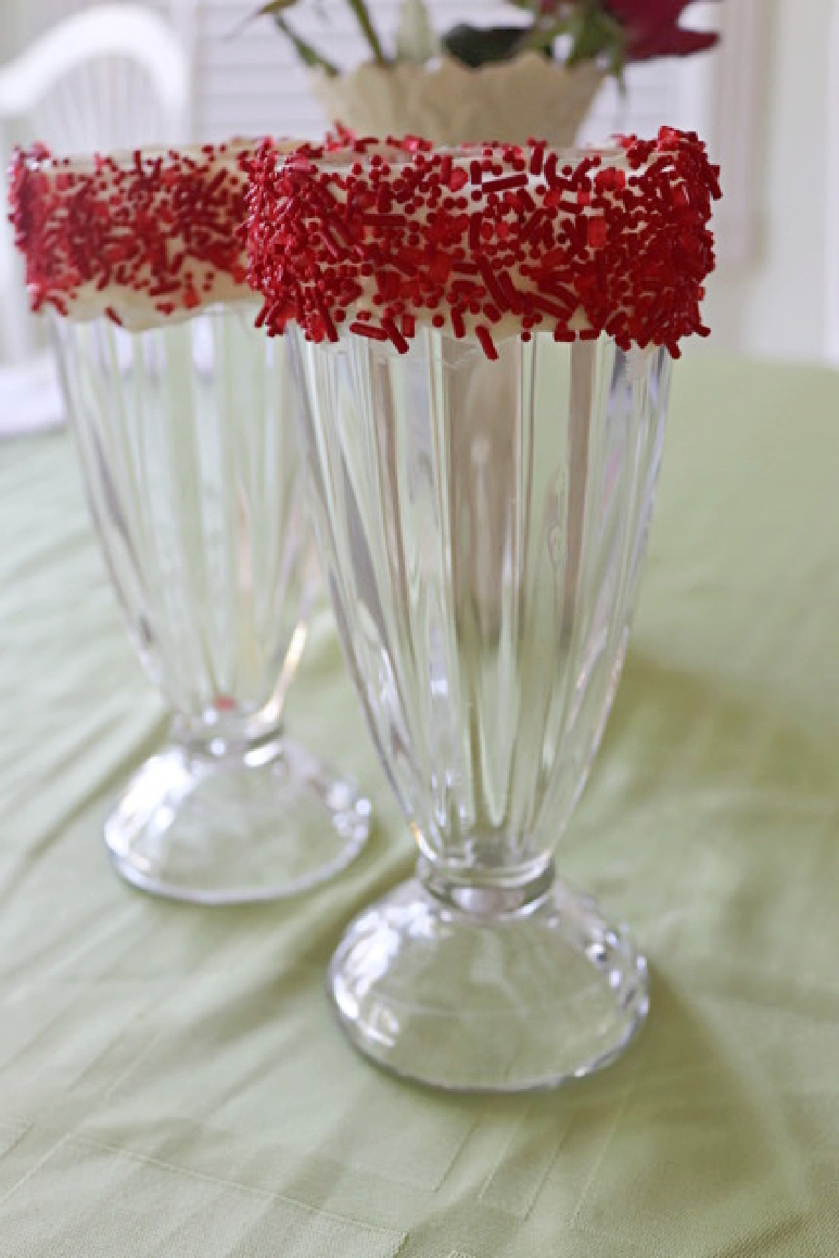Two empty milkshake glasses decorated with white chocolate and red sprinkles.