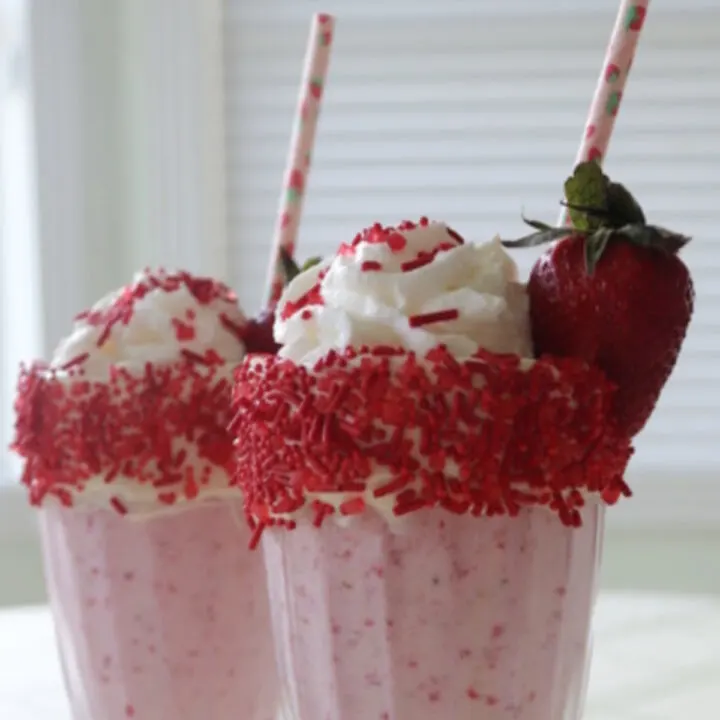 Two strawberry milkshakes with whipped cream and sprinkles garnished with a strawberry.