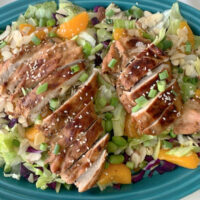 Overhead photo of grilled teriyaki chicken salad on a blue platter.