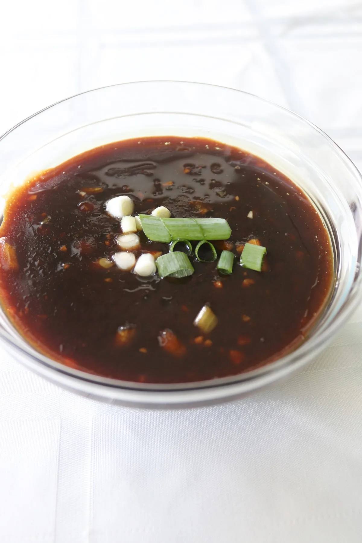 Homemade teriyaki sauce in a clear bowl on a white tablecloth.