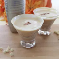 Two white chocolate pumpkin spice martinis with a cocktail shaker on a board.