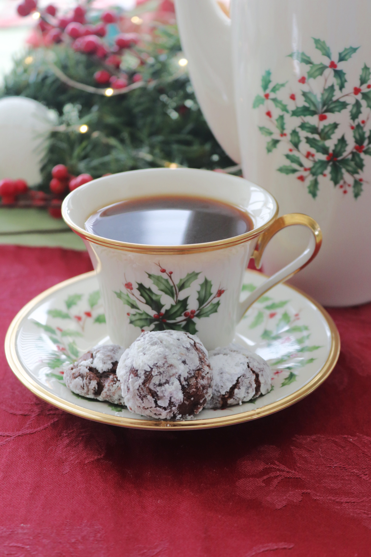 Three chocolate cookies on a saucer next to a holiday cup.