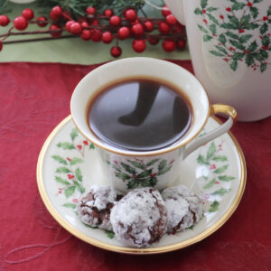 A coffee cup and saucer with holly leaves and 3 peppermint chocolate cookies on the saucer.