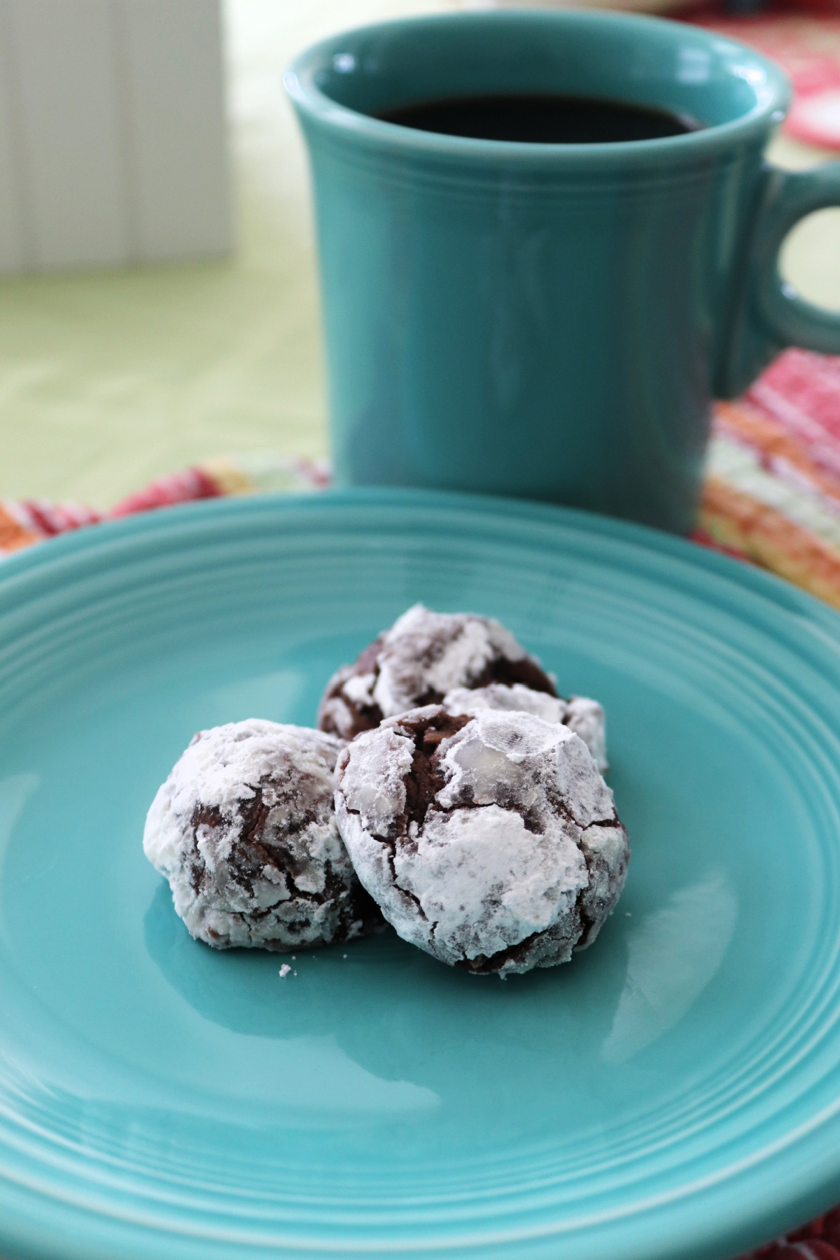 Three powdered sugar chocolate cookies on a green plate.