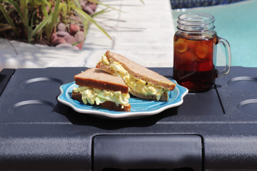 A sandwich on a plate on top of a cooler with a glass of tea.