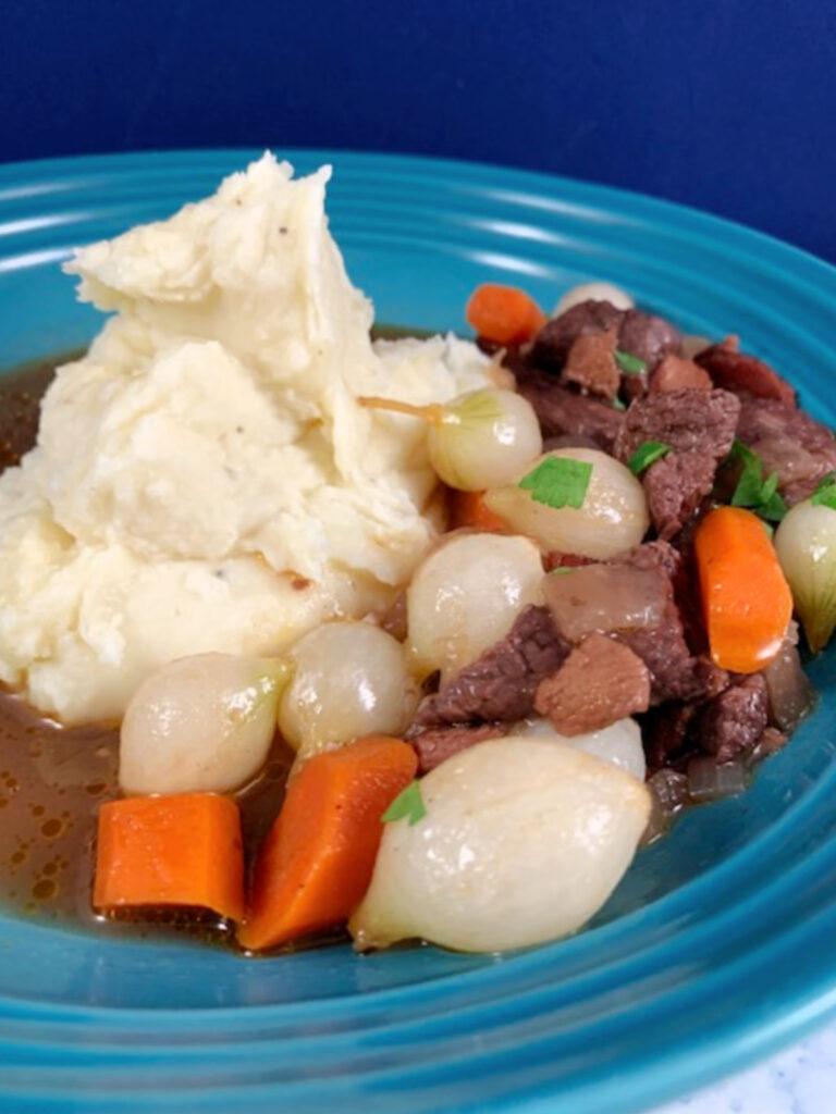 A beef stew with mashed potatoes on a blue plate.