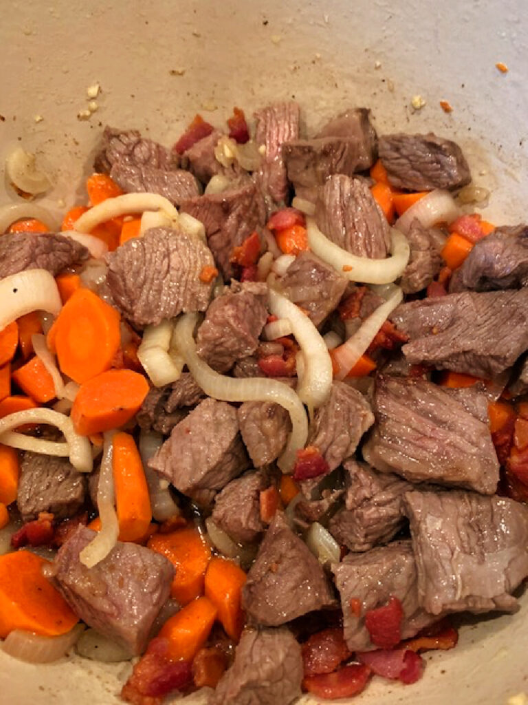 Beef, onions, bacon and carrots in a pot.